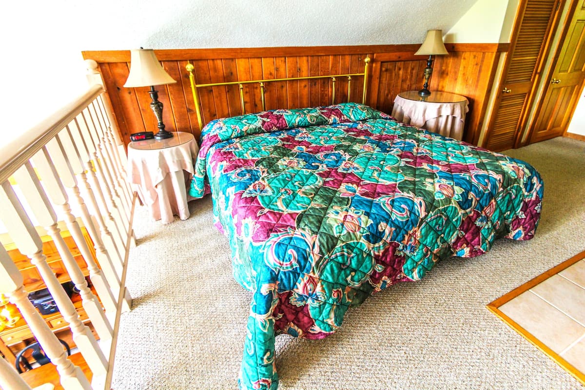 Un dormitorio con una cama, dos mesitas de noche, cabecero de madera y barandilla de balcón.
