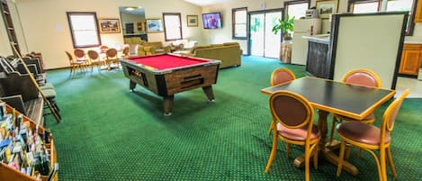 A pool table in a room with green carpeting, a sofa, and a television.