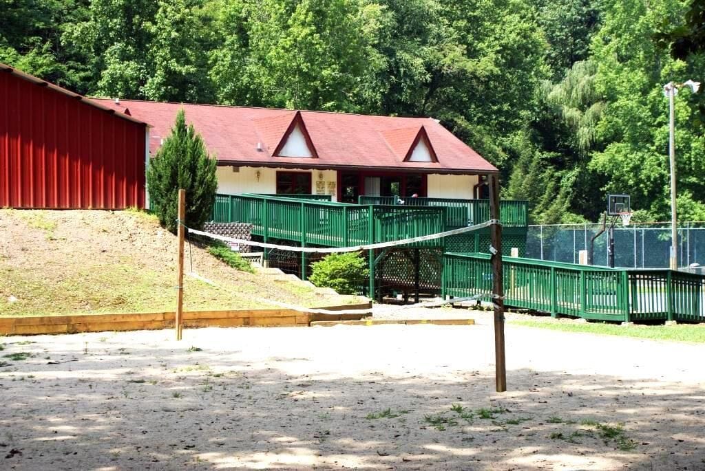 A building with a red exterior and a green roof, a covered walkway, and a basketball court.