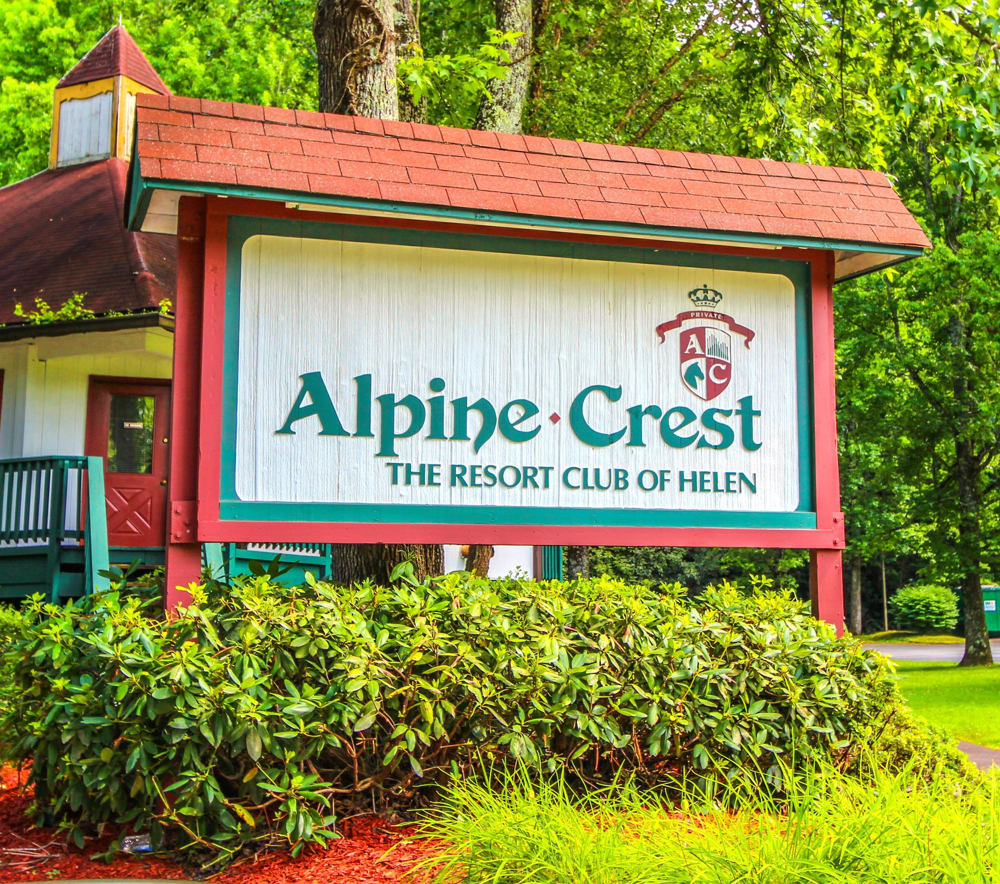 Un letrero para Alpine Crest, The Resort Club of Helen, con techo rojo y detalles verdes.