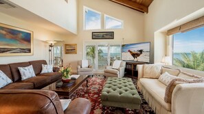 Un salón amplio con un gran ventanal, un televisor de pantalla plana y vistas a la playa.