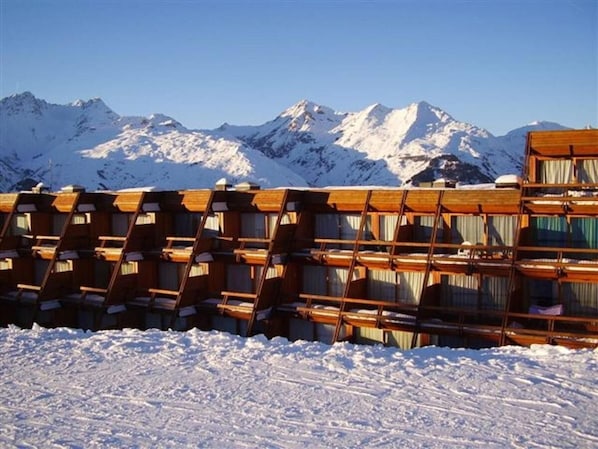 A row of wooden cabins with a snowy mountain backdrop.