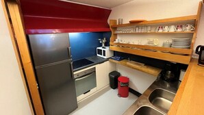 A compact kitchen with a refrigerator, microwave, stove, sink, and a red trash bin. - 50m from ski slopes, 2nd floor, view ski slopes, balcony, tv, 60m², Les Arcs (Bourg-Saint-Maurice)