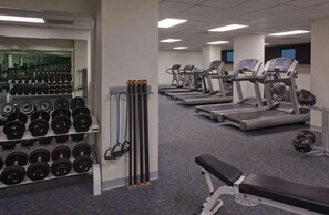 Un gimnasio con cintas de correr, mancuernas y un banco.