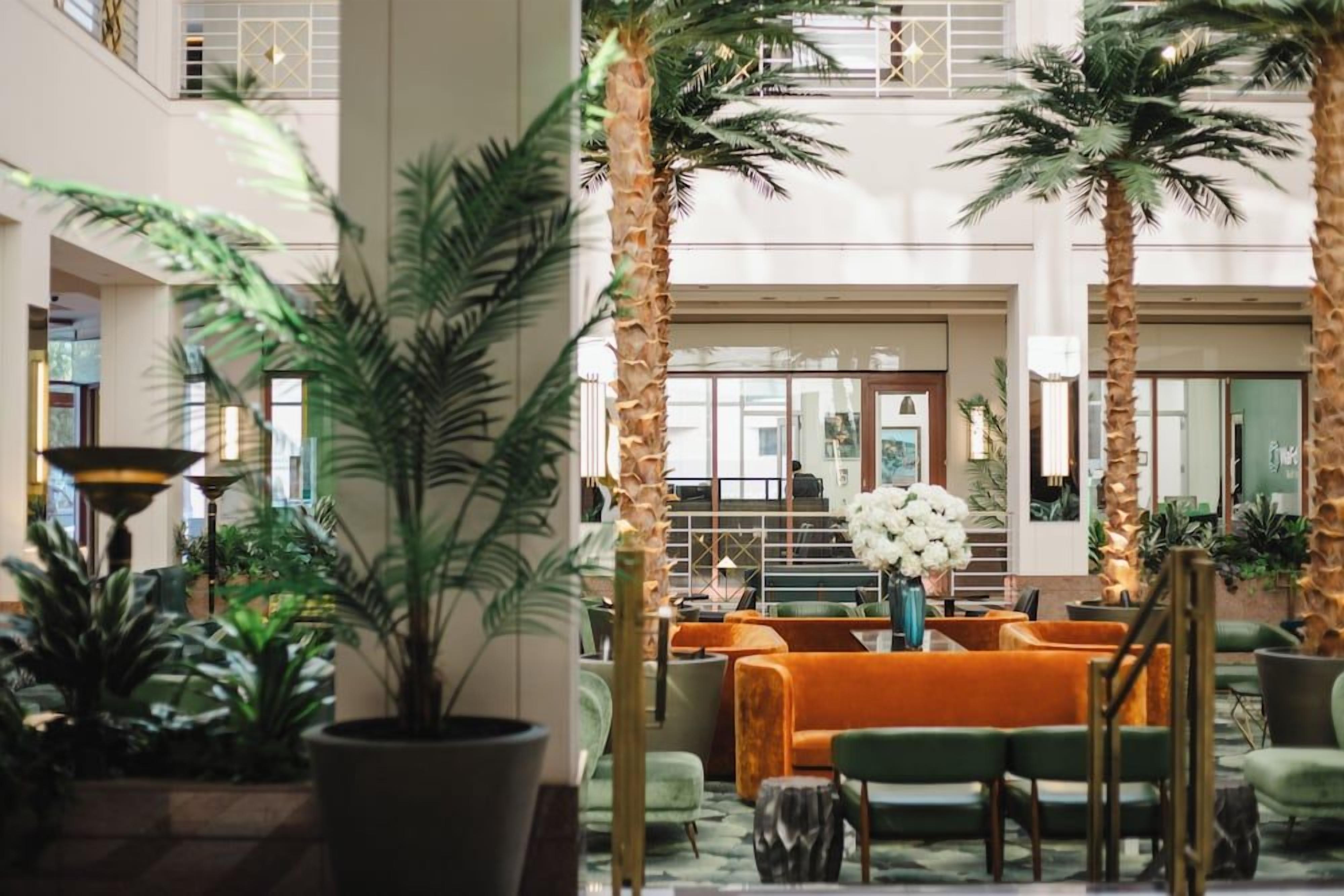 A lobby with a central seating area, palm trees, and a staircase.