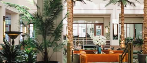 A lobby with a central seating area, palm trees, and a staircase.