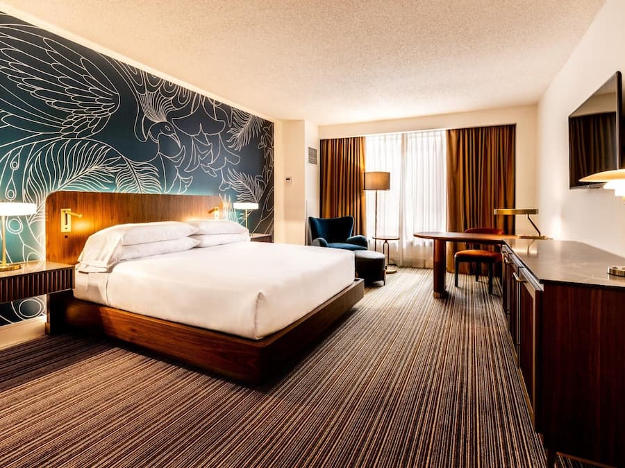 Habitación de hotel con una cama grande, un escritorio, una silla, un televisor y una pared con diseño de hojas.