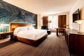 Habitación de hotel con una cama grande, un escritorio, una silla, un televisor y una pared con diseño de hojas.
