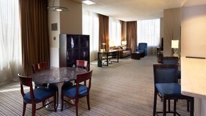 Una habitación de hotel con una mesa de comedor, sillas, un sofá, un televisor y una lámpara.