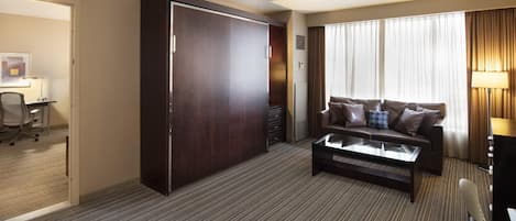 A hotel room with a large wardrobe, a sofa set, a coffee table, and a desk with a lamp.