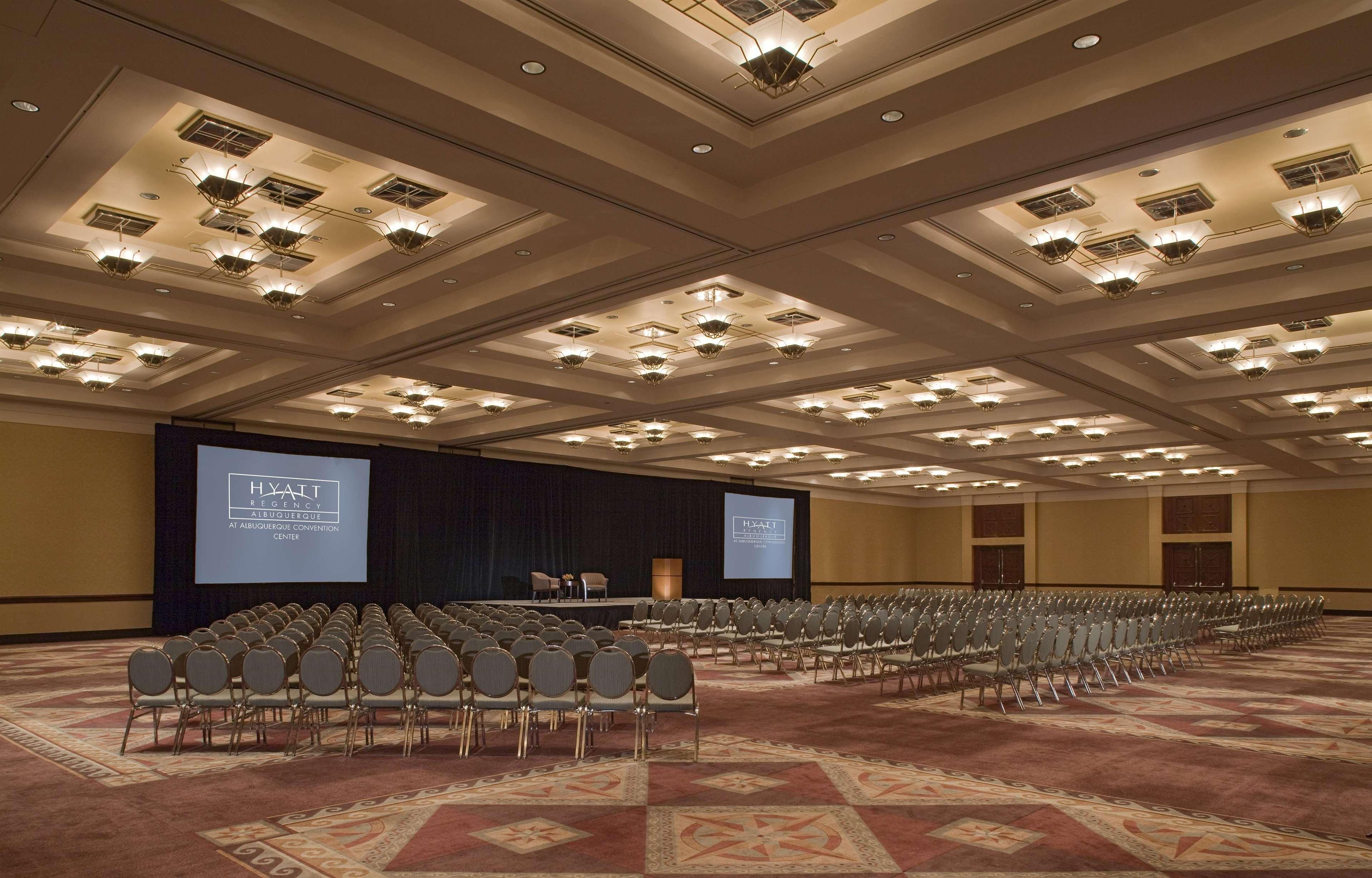 Une grande salle de conférence, avec des rangées de chaises, une scène et un grand écran affichant le nom « Hyatt Regency ».