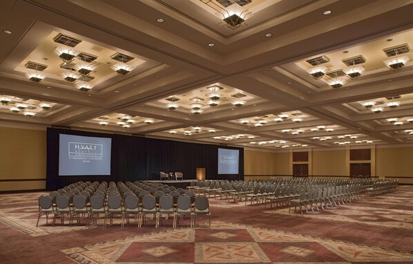 Een ruime congreszaal met rijen stoelen, een podium en een groot scherm waarop 'Hyatt Regency' staat.