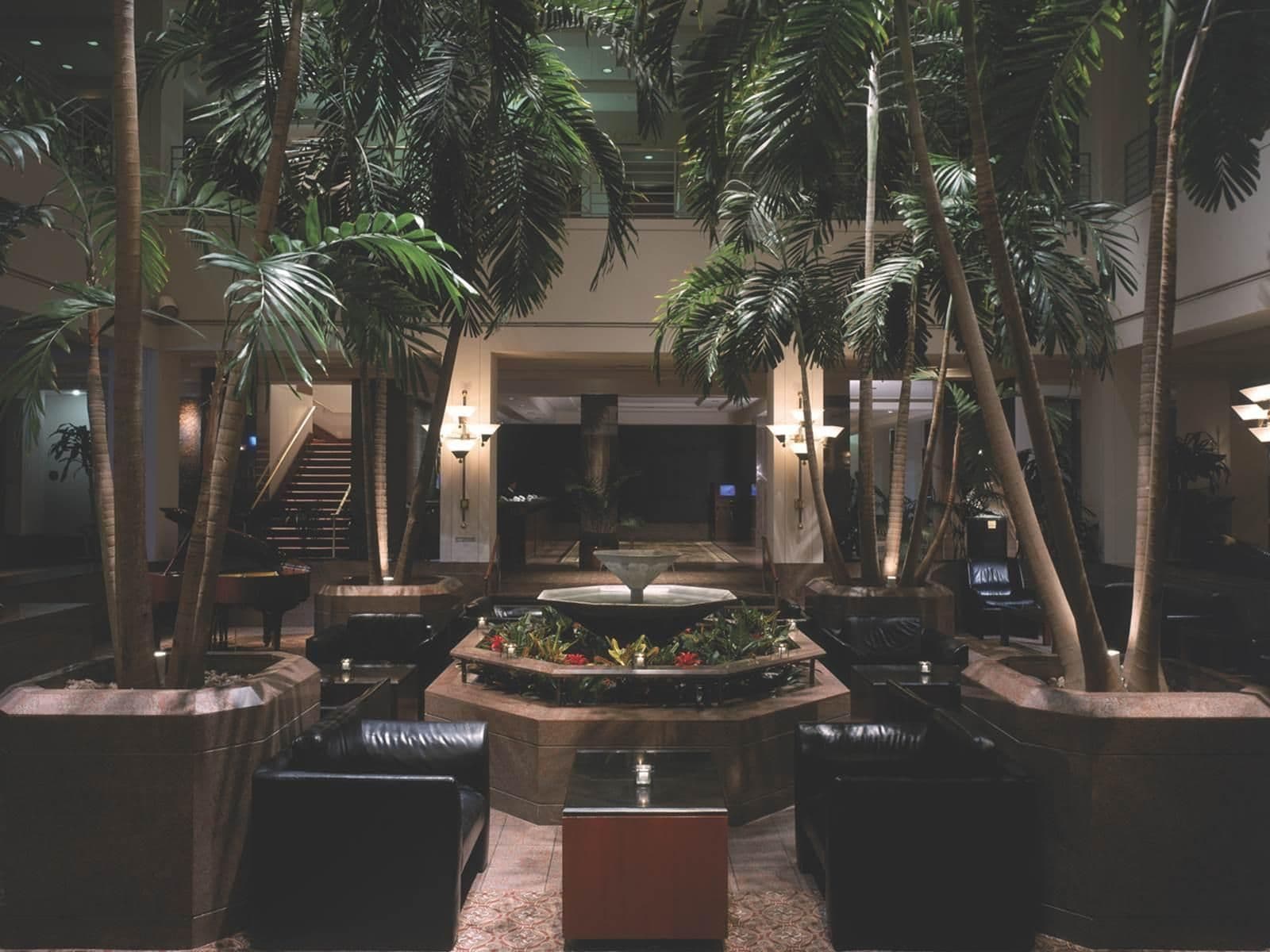 A lobby with a central water feature, multiple seating areas, and tall palm trees.