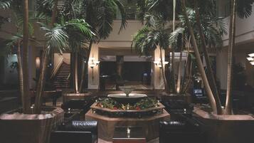 A lobby with a central water feature, multiple seating areas, and tall palm trees.