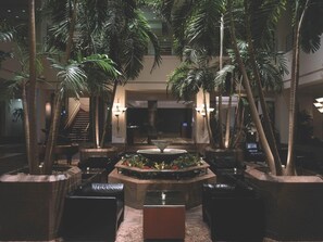 A lobby with a central water feature, multiple seating areas, and tall palm trees. - The Clyde Hotel (Albuquerque)