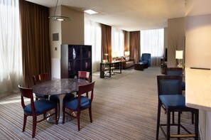 A hotel room with a dining table, chairs, a sofa, a TV, and a lamp. - The Clyde Hotel (Albuquerque)