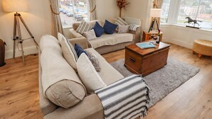 A cozy living room with a sofa, a wooden coffee table, and a view of the street through large windows. - White Horses (Whitby)