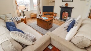 A living room with a fireplace, sofa, television, and a view of the city through large windows. - White Horses (Whitby)
