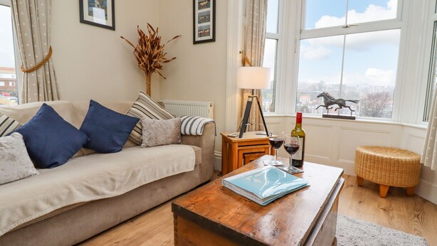 A cozy living room with a sofa, a wooden coffee table, and a view of the city through large windows. - White Horses (Whitby)