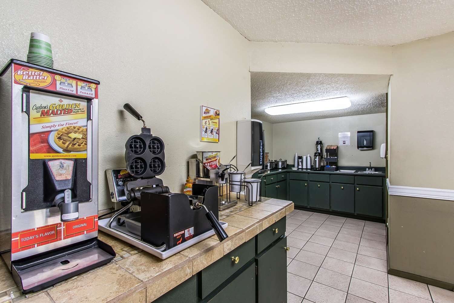 A kitchen with a waffle maker, a coffee machine, and a syrup dispenser.