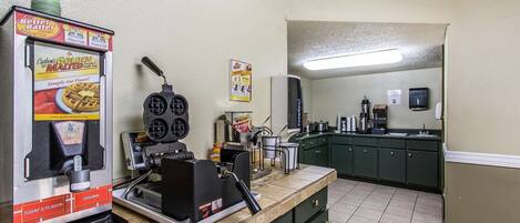 A kitchen with a waffle maker, a coffee machine, and a syrup dispenser.