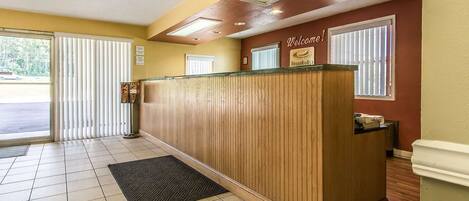 A reception desk with a 'Welcome!' sign, a tiled floor, and a door leading outside.