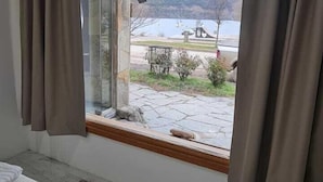 A bedroom with a bed, a window with curtains, and a view of a lake and mountains. - PUERTO LACAR LODGE SMARG (San Martín de los Andes)