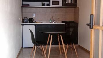 A compact kitchen with a black table and chairs, a microwave, and a small stove.