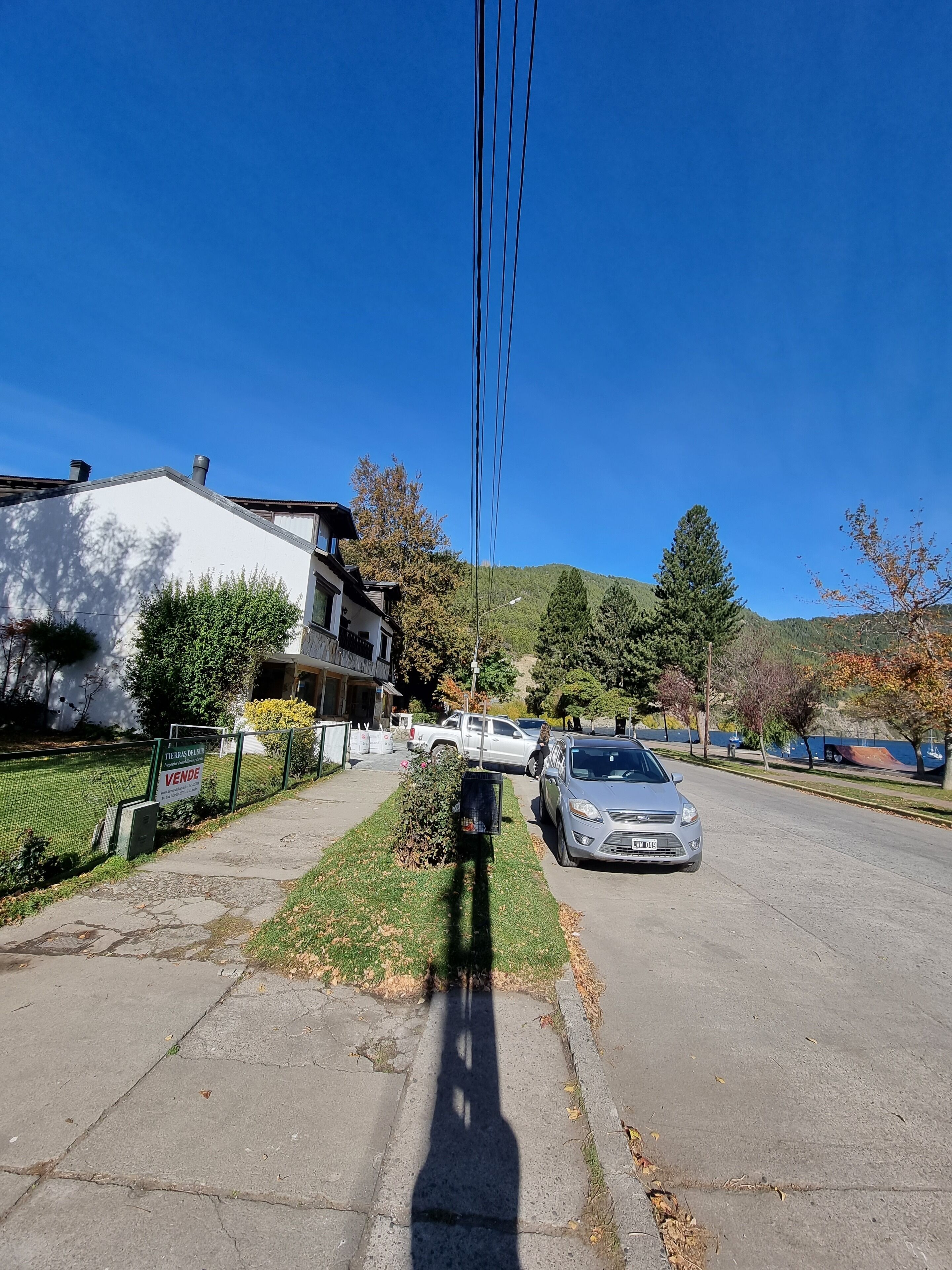Rua residencial com casas, um carro estacionado e céu azul.