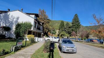 Rua residencial com casas, um carro estacionado e céu azul.