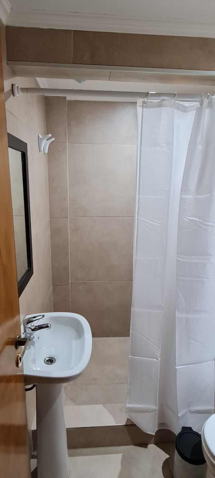 Un baño con un lavamanos blanco, cortina de ducha y piso de baldosas.