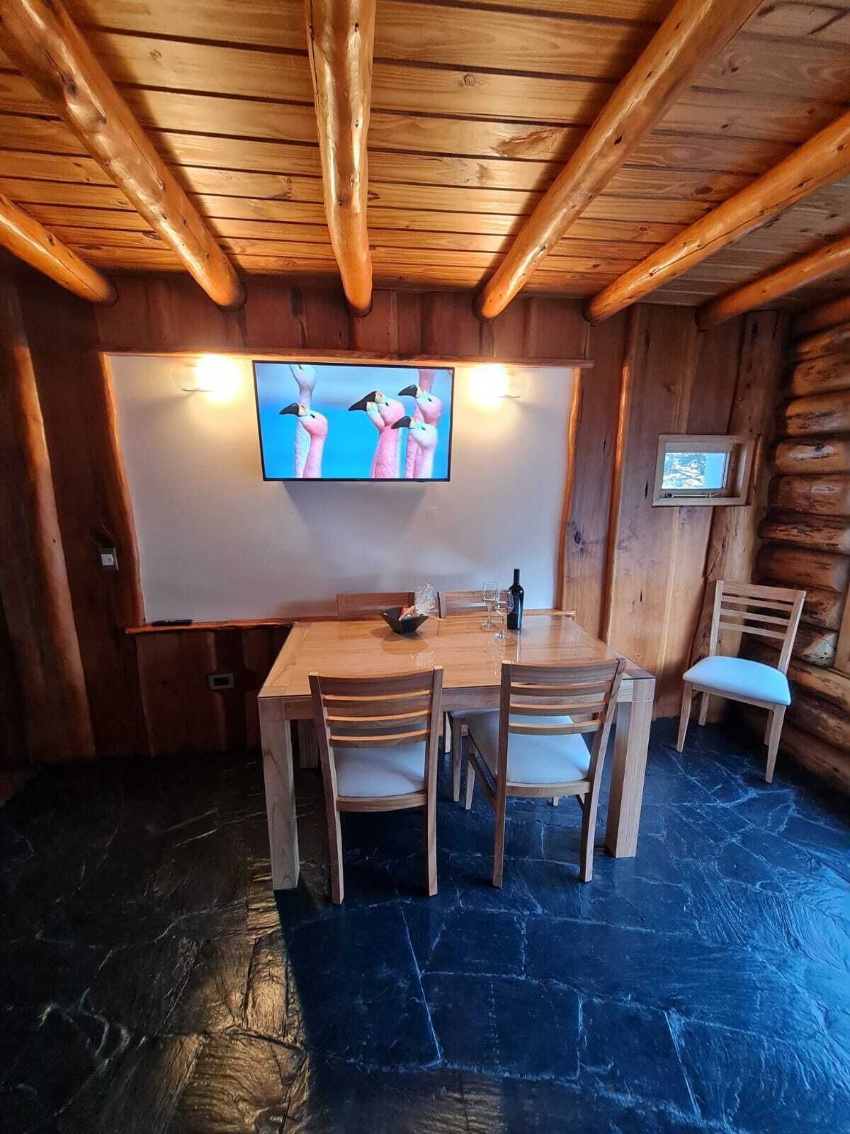 A wooden dining area with a stone floor, a television mounted on the wall, and a small table with chairs.