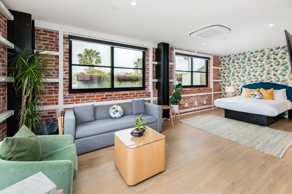 A modern living room with a grey sofa, a green armchair, a wooden coffee table, and a bed with a blue headboard.