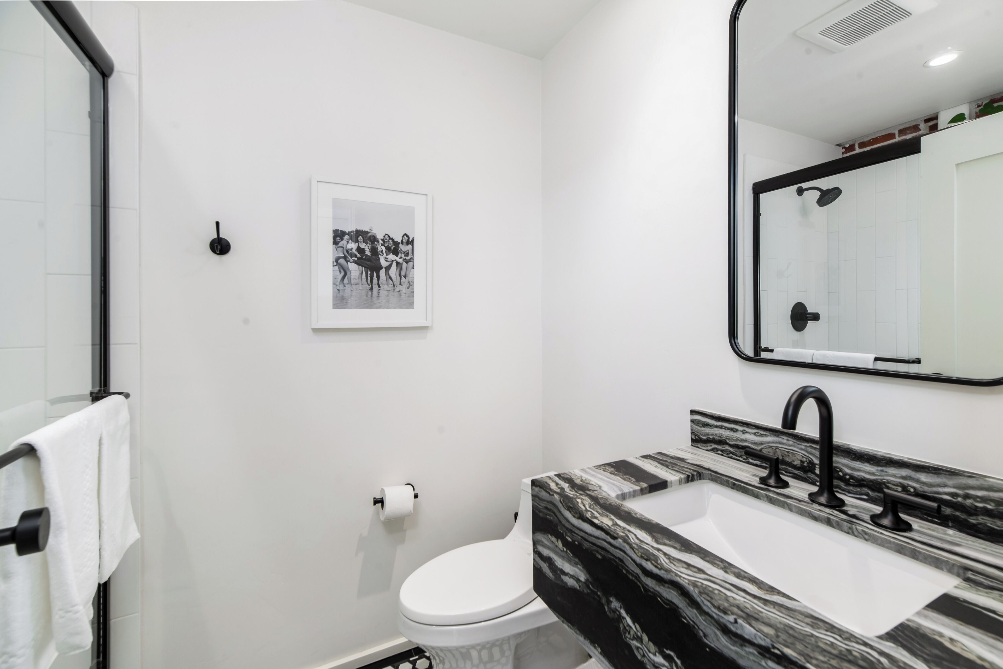 Un baño moderno con inodoro blanco, lavamanos de mármol blanco y negro, y una fotografía enmarcada en la pared.