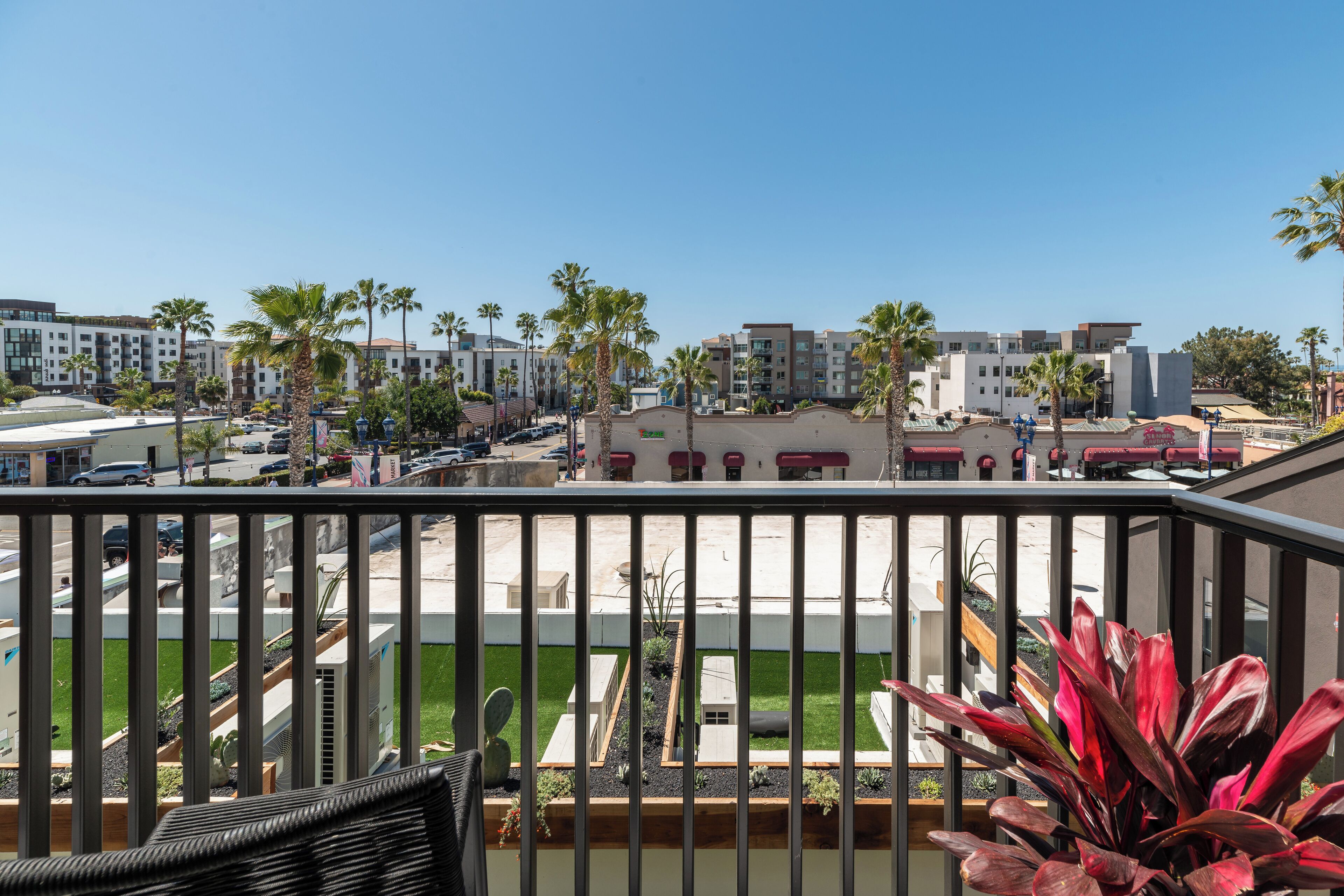 A balcony with a view of a parking lot, palm trees, and modern buildings.