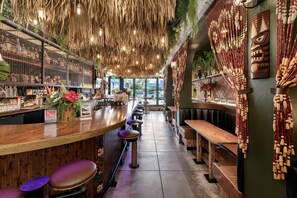 A bar area with wooden bar counters, stools, and a seating area with benches. - The Brick Hotel (Oceanside)