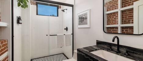 A modern bathroom with a glass-enclosed shower, a black marble sink, and a white toilet.