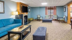 A hotel room with a blue sofa, a small table with a lamp, a television, and a patterned carpet. - Suburban Studios Chester I-95, VA (Chester)