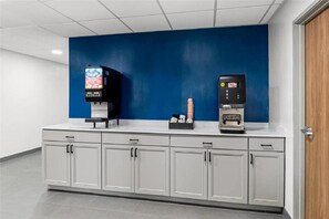 Un angolo dedicato alle bevande self-service, con due distributori, una parete blu e un bancone bianco con pensili.