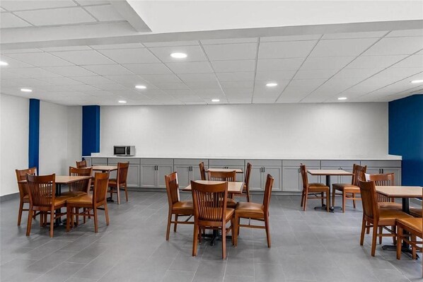 A spacious dining area with multiple wooden tables and chairs, a microwave, and grey cabinets. - Suburban Studios Chester I-95, VA (Chester)