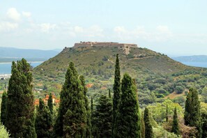 A hilltop fortification overlooking a coastal area with dense greenery and a few buildings in the foreground. - Pimpinnacolo - 2BR P5 (Monte Argentario)