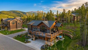 Une grande cabane en bois dotée d’une terrasse et d’un jacuzzi, entourée d’arbres et de montagnes.