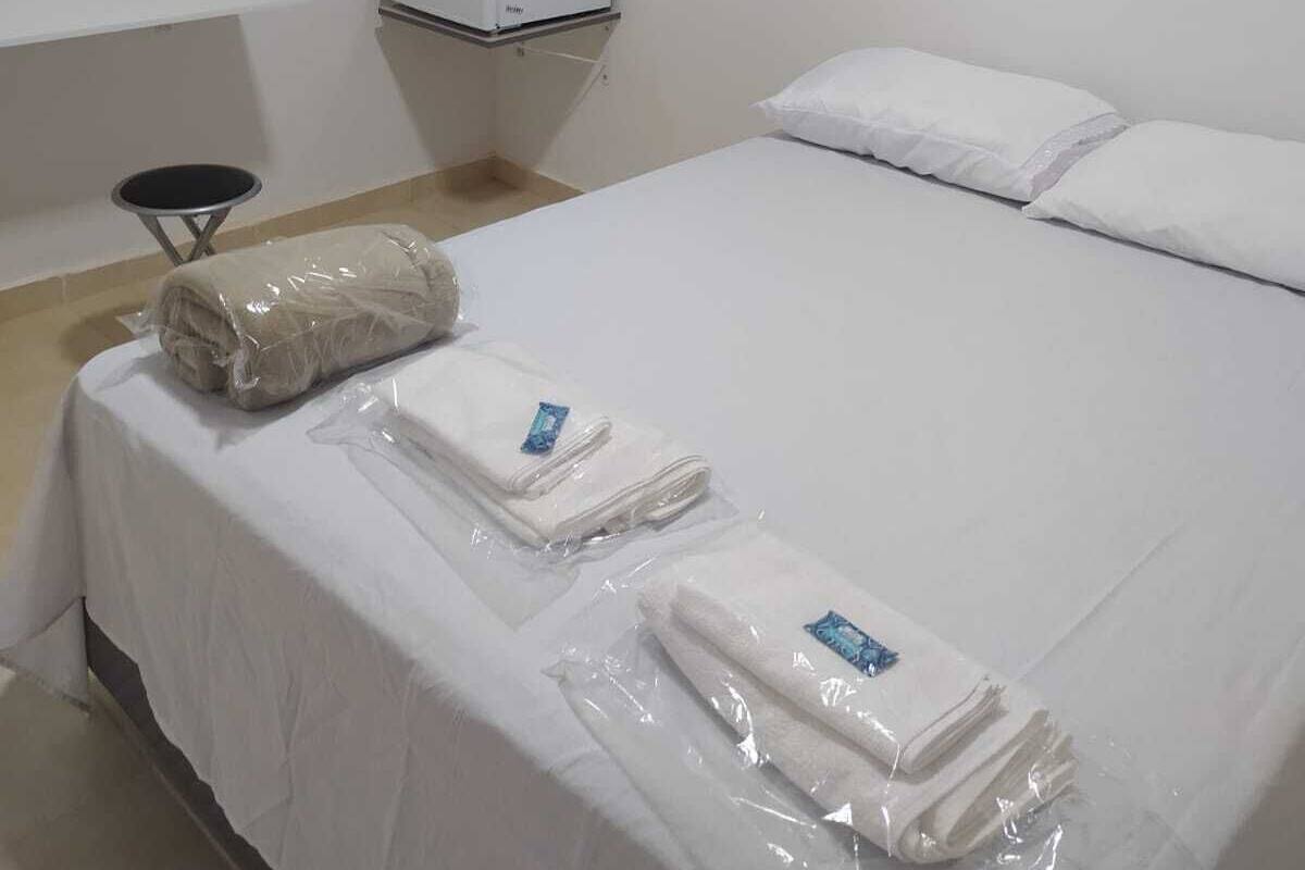 A hotel room with a bed, a small desk, a white wardrobe, and a window.