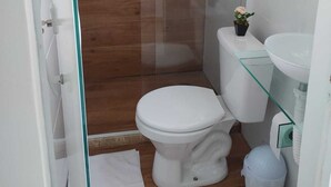 Un baño pequeño y moderno con cabina de ducha de vidrio, inodoro blanco y lavamanos de vidrio.