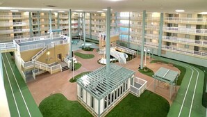 Ein mehrstöckiges Hotel mit zentralem Atrium, Außenbereichen zum Sitzen und einem Pool.