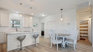 A modern kitchen with white cabinetry, a central island with bar stools, and pendant lighting. - Beach Cottage with a View!! (Gulfport)