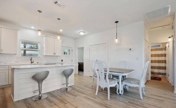 Une cuisine moderne avec des meubles blancs, un îlot central doté de tabourets et des luminaires suspendus.