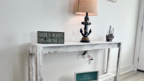 A rustic wooden console table with a sign that reads "THERE'S ALWAYS TIME FOR THE SEA," a lamp, a small ship model, and a decorative whale figurine. - Beach Cottage with a View!! (Gulfport)