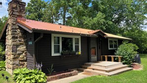 Een chalet met een stenen schoorsteen, een rood dak en een veranda met treden naar de deur.