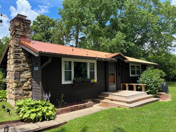 Eine Holzhütte mit einem Steinkamin, einem roten Dach und einer Veranda mit Stufen zum Eingang.